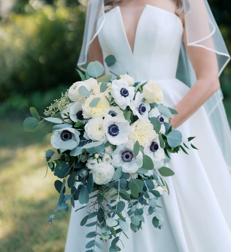 Bride holding a cascading bouquet of white blooms and eucalyptus greenery in a modern wedding gown. Fearrington Village.