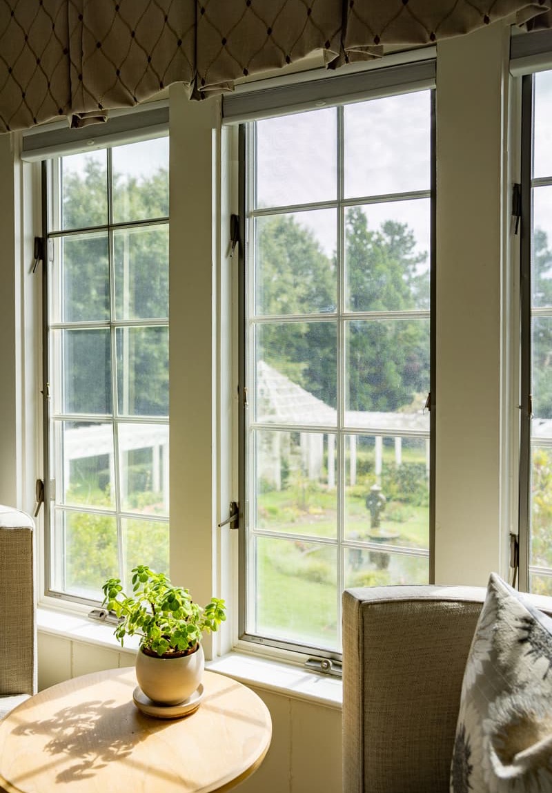 Sunlit seating area at The Fearrington House Inn overlooking lush gardens through tall windows. Fearrington Village.