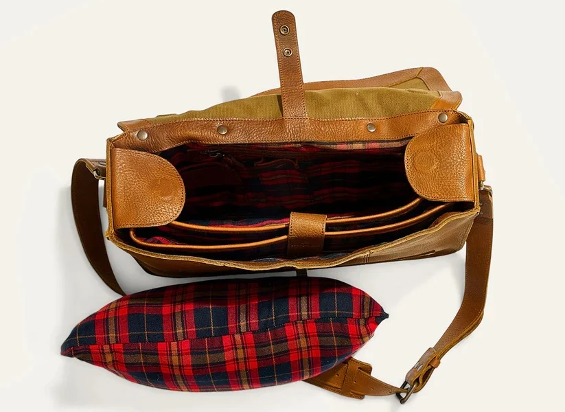Open tan leather messenger bag showing a red plaid interior, padded compartments. Fearrington Village.