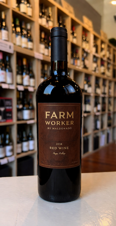 Bottle of Farm Worker by Maldonado 2018 red wine on a counter, with wine shelves in the background.