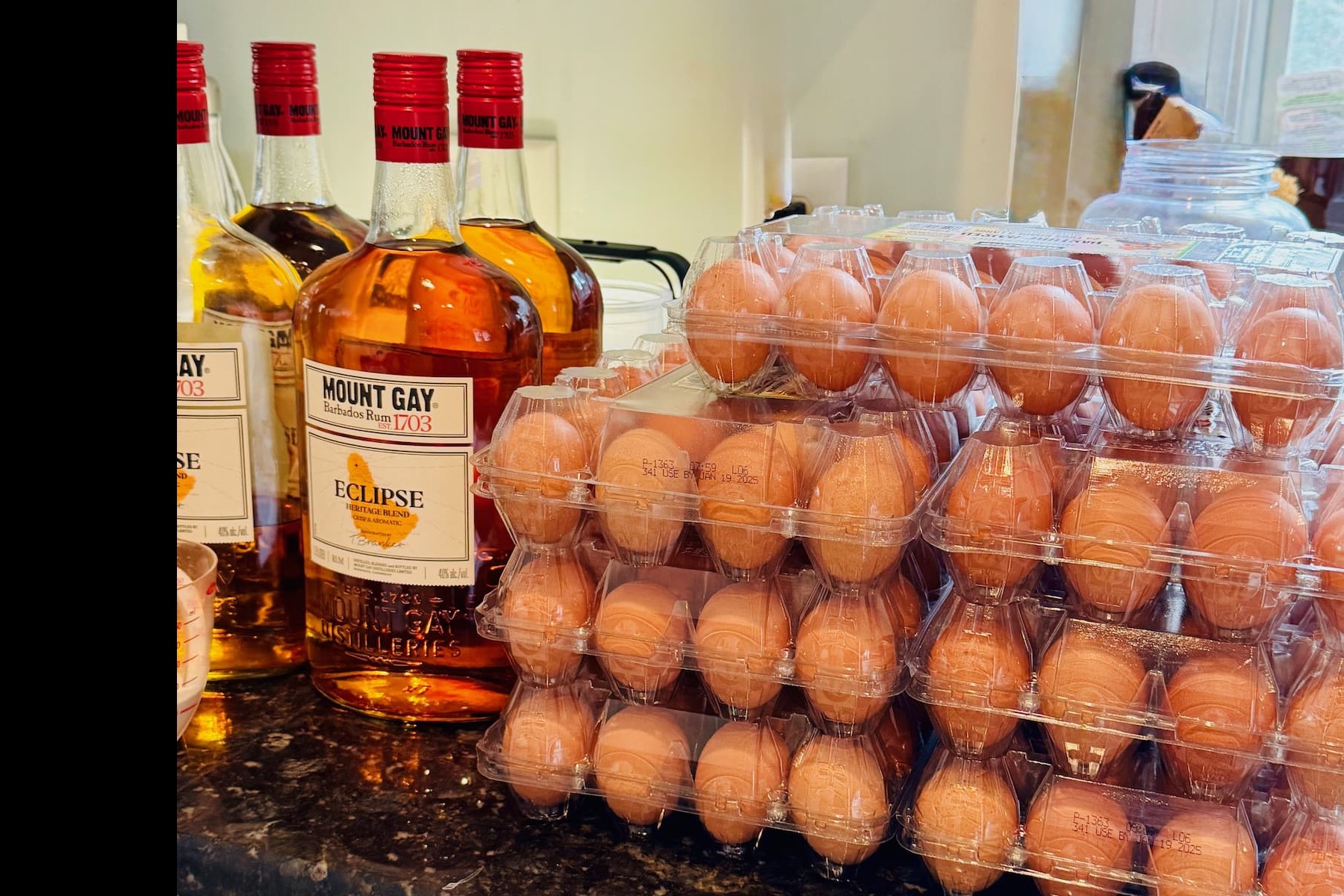 Stacked cartons of eggs sit on a kitchen counter beside several bottles of Mount Gay Eclipse rum.
