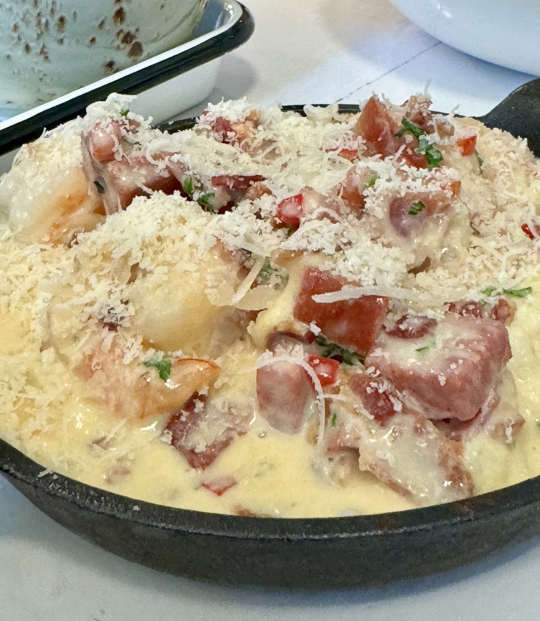 Three-tier afternoon tea stand with pastries, scones, and finger sandwiches set on a white tablecloth, with teapot, teacups, and window light in the background.