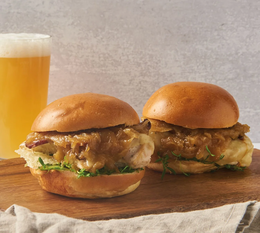 Two gourmet chicken sandwiches topped with caramelized onions and melted cheese on brioche buns, served with a pint of beer. Fearrington Village.