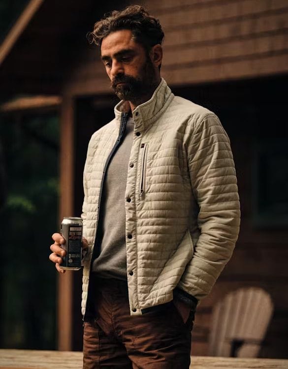Man wearing a light quilted jacket over a gray sweater in a relaxed outdoor setting. Fearrington Village.