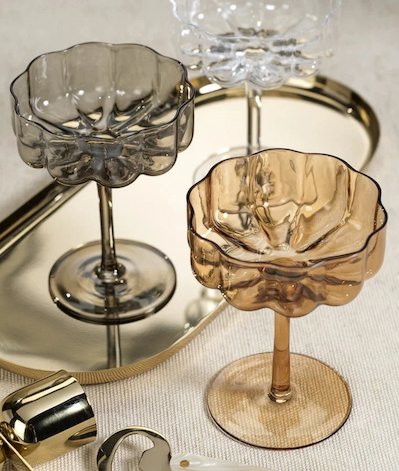 Amber, smoky gray and clear scalloped coupe glasses arranged on a reflective gold tray with cocktail accessories. Fearrington Village.
