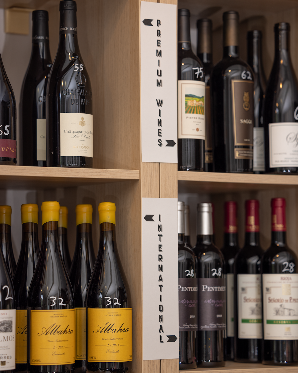 Shelves of wine bottles organized by section, with signs marking “Premium Wines” and “International” in a wood display at the bottle shop.