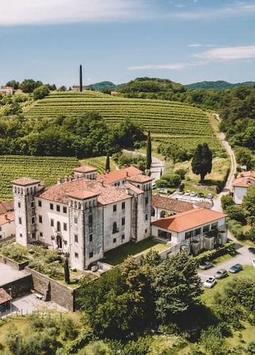 Model wearing a loose, ankle-length dress with wide three-quarter sleeves and a V-neckline, featuring a vibrant multicolor paisley and floral print in turquoise, coral, yellow, and pink tones, paired with light blue open-toe sandals against a neutral studio background.