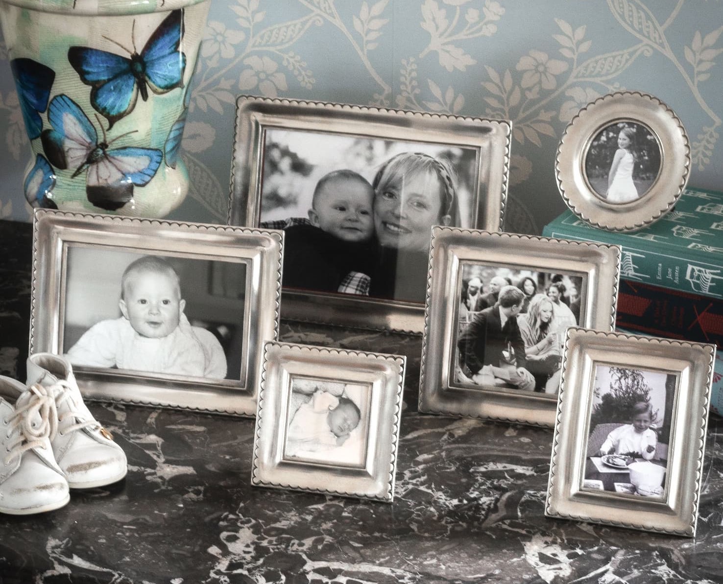 Silver photo frames in assorted sizes displaying family photographs, styled on a marble-topped dresser with a butterfly-patterned jar. Fearrington Village.