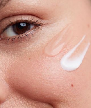 Close-up of a person’s cheek with two swipes of face cream applied near the eye.
