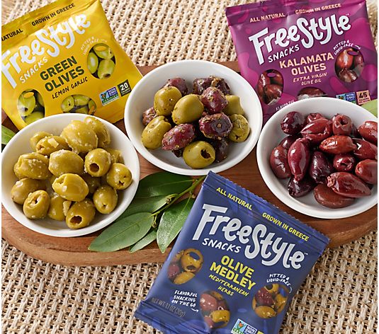 Three bowls of marinated olives surrounded by colorful Freestyle Snacks olive pouches, styled on a woven tabletop with fresh leaves and a casual Mediterranean-inspired presentation.