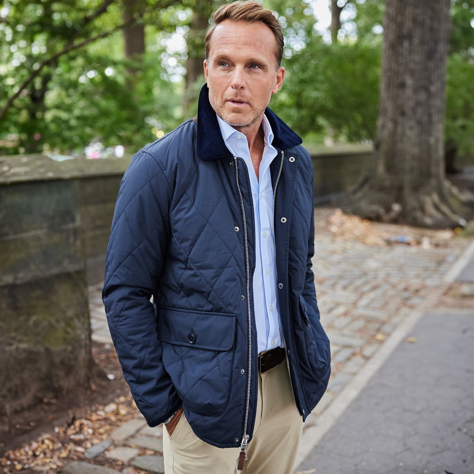 Man wearing a navy quilted jacket over a light blue shirt and khaki trousers outdoors. Fearrington Village.