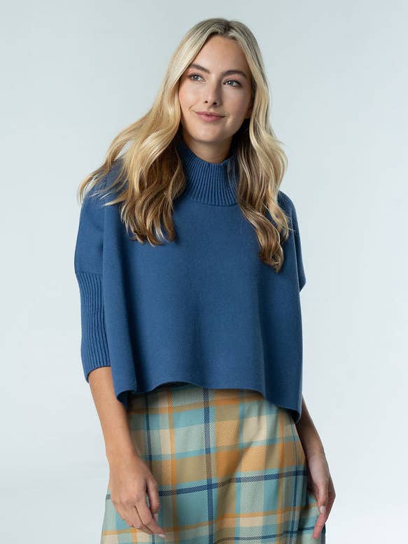 A woman models a cropped blue mock-neck sweater with three-quarter sleeves, paired with soft blue, tan and gold plaid pants. Fearrington Village.
