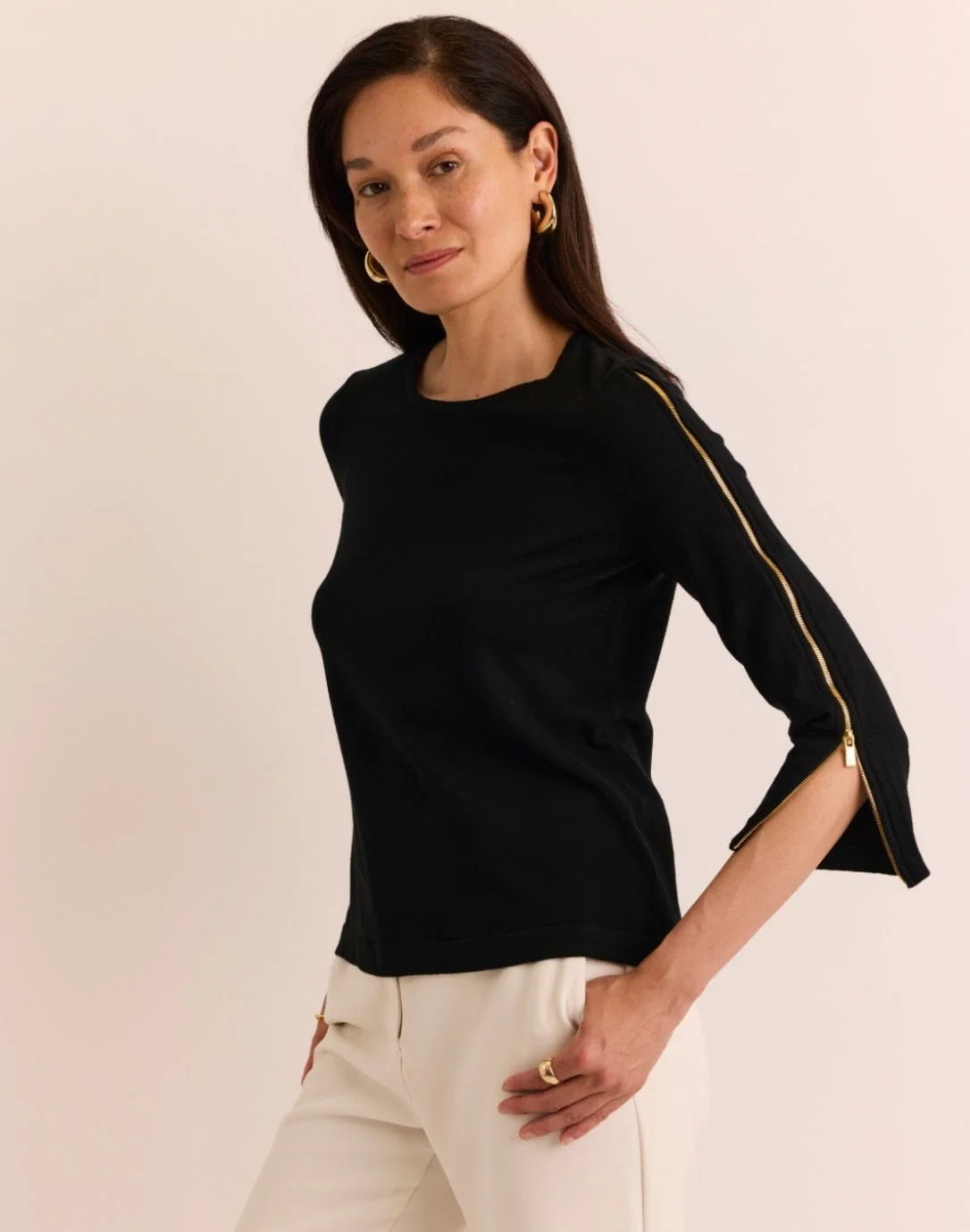 Woman modeling a black three-quarter-sleeve top with gold zipper details along the sleeves, paired with ivory pants. Fearrington Village.