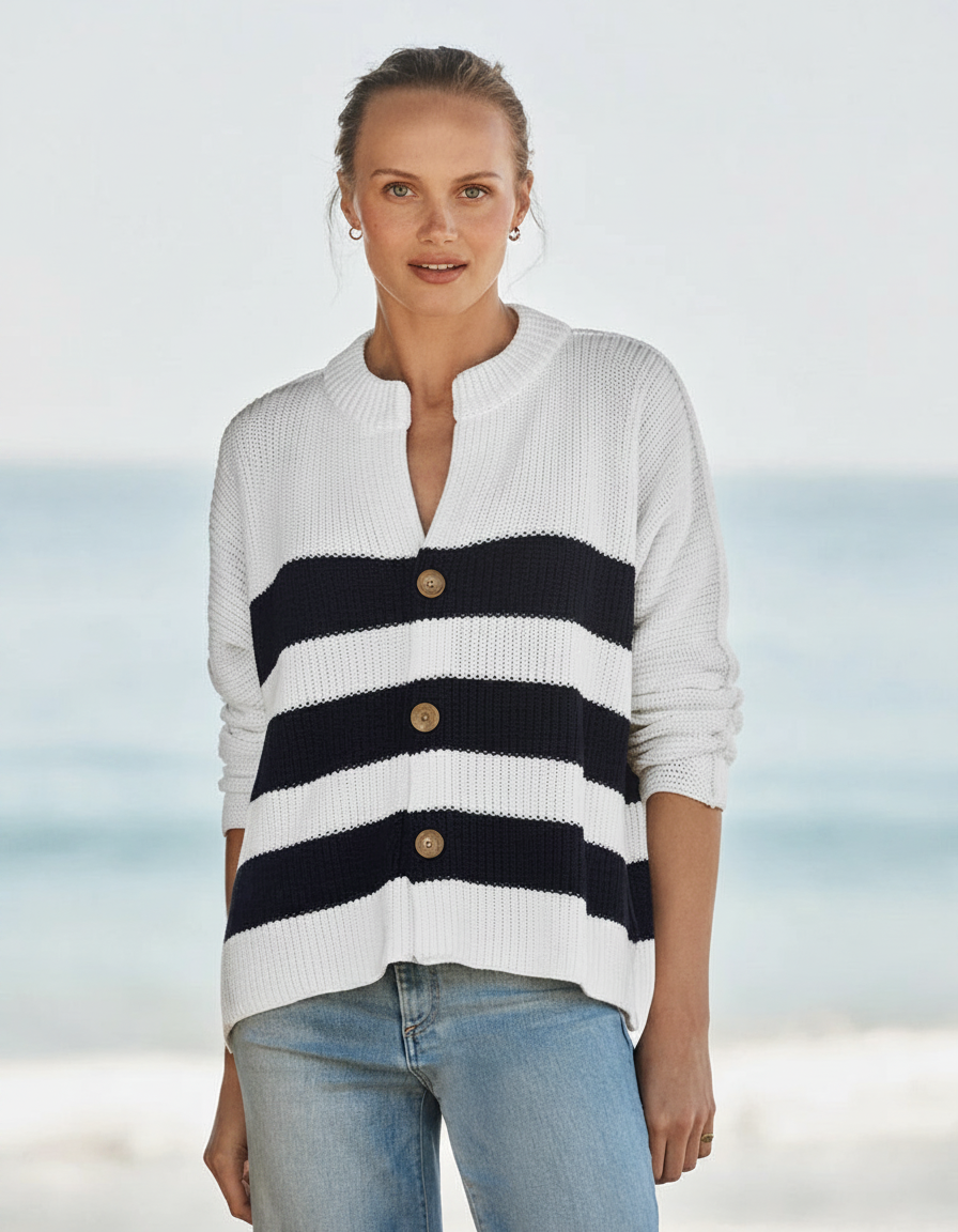Woman in a striped sweater and jeans stands on a beach.