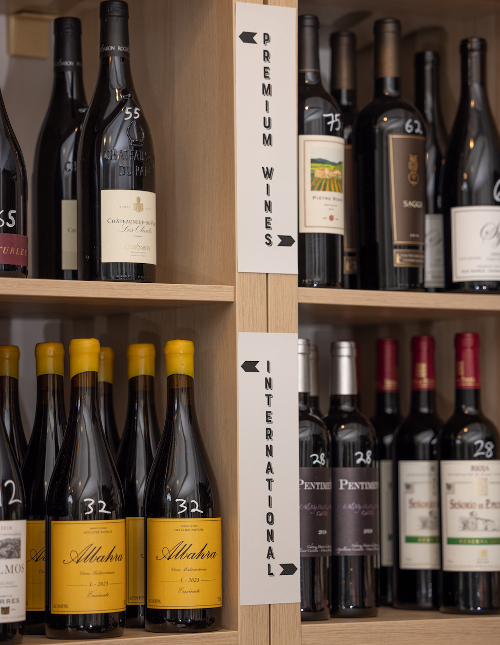 Shelves of wine bottles organized by section, with signs marking “Premium Wines” and “International” in a wood display at the bottle shop.