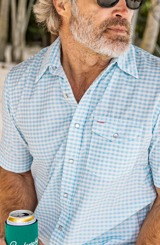 Man wearing sunglasses and a light blue gingham short-sleeve button-down shirt, holding a drink can outdoors.