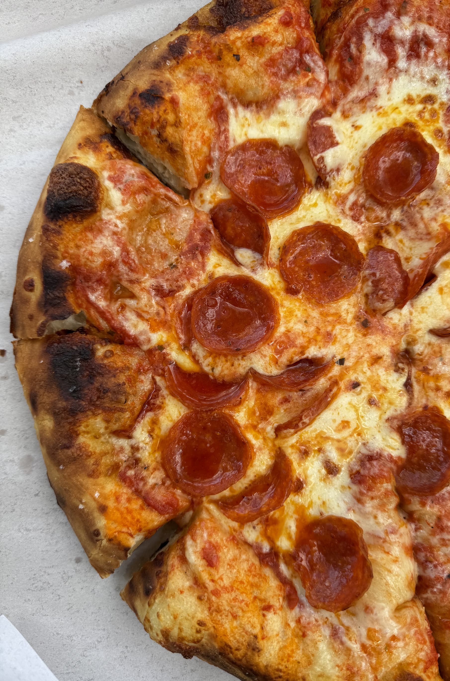 Close-up of a pepperoni pizza with melted cheese and a charred, bubbly crust, sliced into wedges on parchment paper.