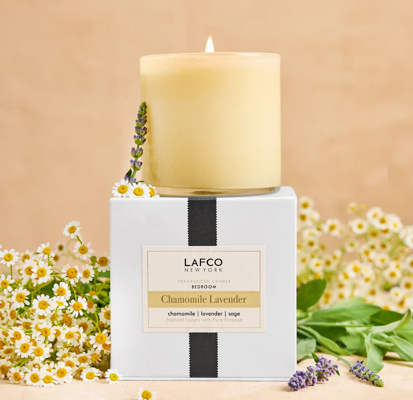 Pale yellow glass candle labeled “LAFCO New York Chamomile Lavender,” displayed on its box with chamomile flowers and lavender against a warm neutral background.
