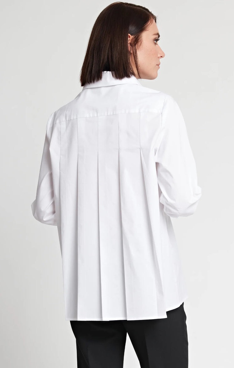 A woman with short brown hair wears a white blouse with pleated detailing on the back, shown from a side and rear view against a plain light background.
