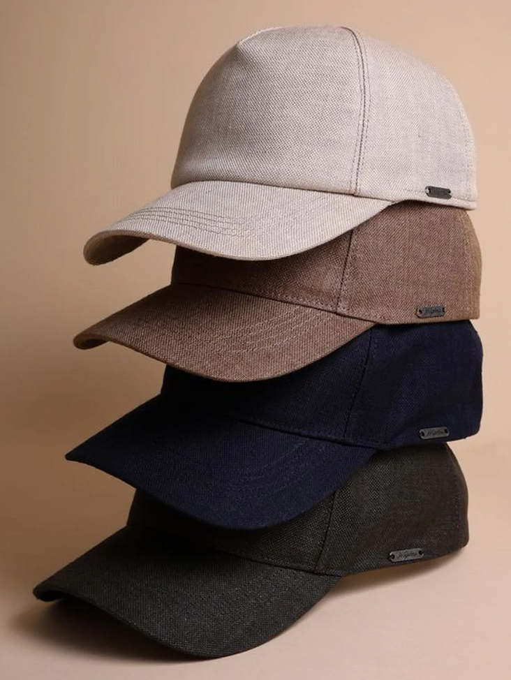 A stack of five textured caps in neutral tones, including beige, brown, navy, and charcoal, displayed against a warm background.