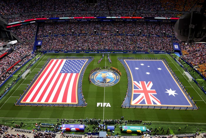 Fans fill a stadium as giant United States and Australian flags are displayed during a FIFA pre-match ceremony.