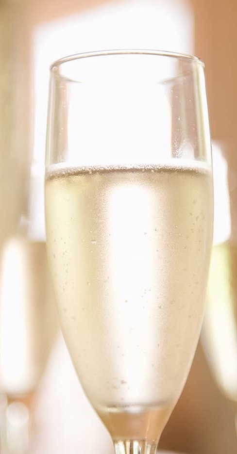Close-up of a flute glass filled with pale sparkling wine, tiny bubbles rising in soft natural light, creating a bright and celebratory atmosphere.