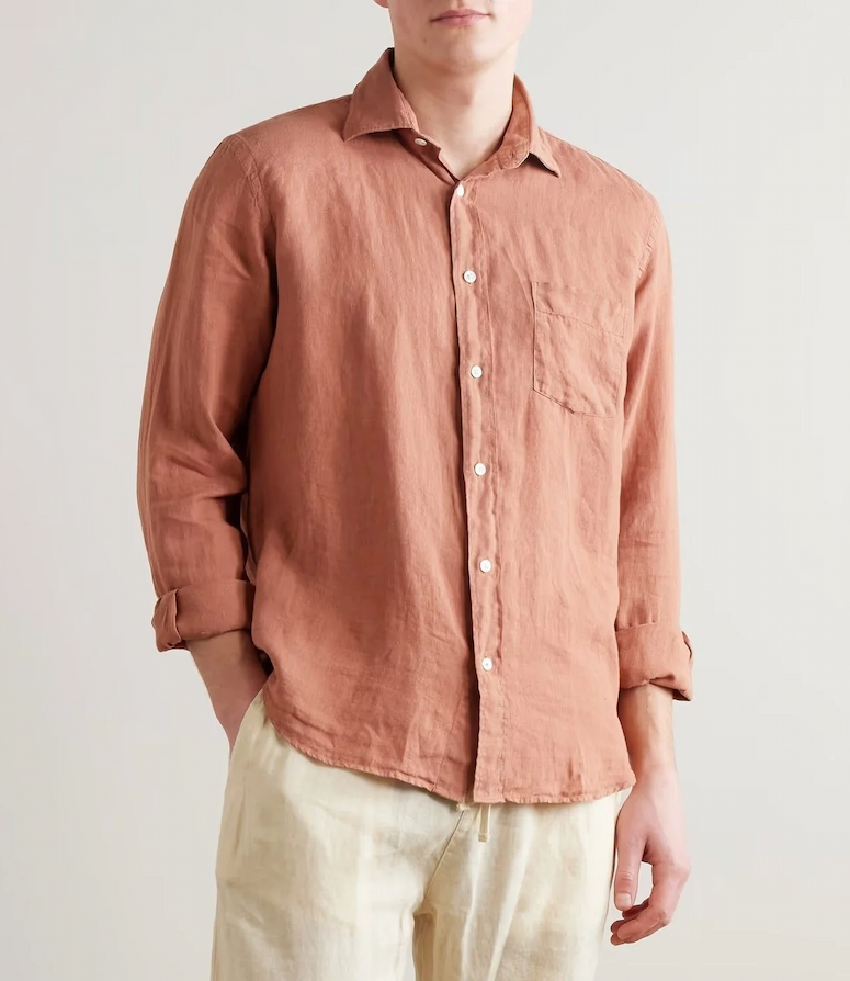 Man in a relaxed, lightweight button-down shirt in a warm terracotta tone, styled with sleeves casually rolled and paired with light, easy trousers.