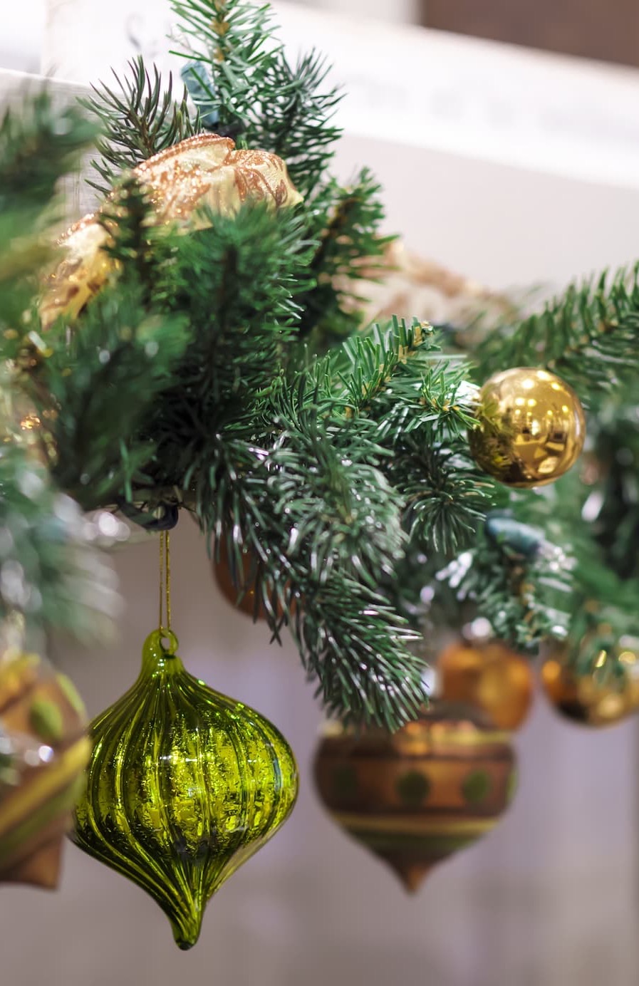 Close-up of a festive Christmas garland decorated with green pine branches and gold and green ornaments, including a shiny, textured green bauble in the foreground. Fearrington Village