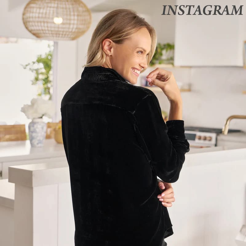 A woman smiles while standing in a bright kitchen, wearing a black velvet top with her back partly turned toward the camera.