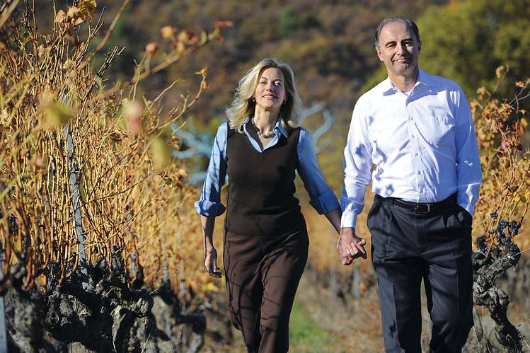 Couple walking hand in hand through a vineyard lined with autumn vines. Fearrington Village.