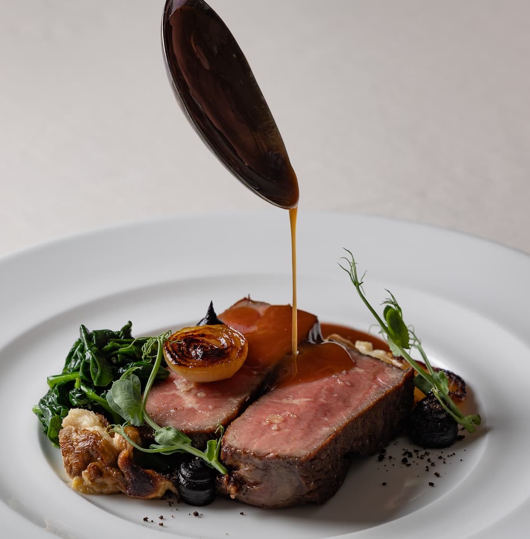Slices of roasted meat with greens and vegetables as a rich sauce is spooned over the dish at The Fearrington House Restaurant. Fearrington Village.