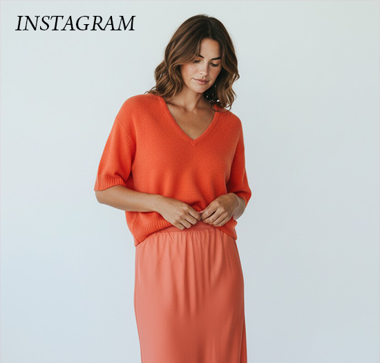 Woman in an orange knit top and matching skirt, looking down with a relaxed expression against a plain background, with the word “Instagram” in the corner.