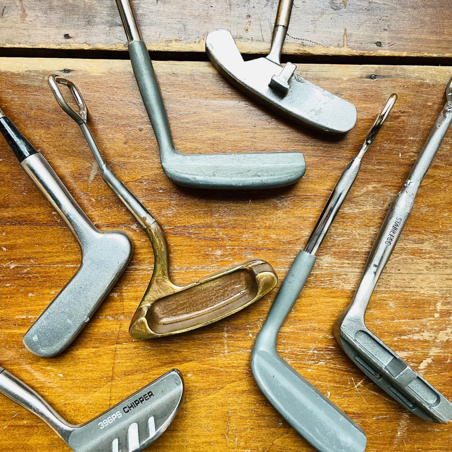 Collection of vintage golf club bottle openers crafted from repurposed golf clubs, displayed on a weathered wooden tabletop. Each opener features a unique club head and polished metal shaft, blending nostalgic golf memorabilia with practical barware.