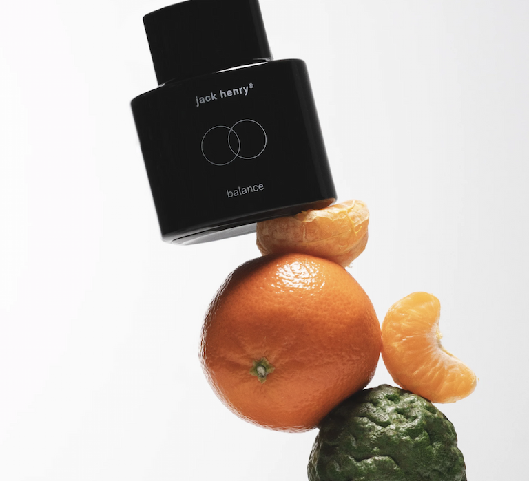 Jack Henry Balance bottle balanced on stacked citrus fruits against a white background.
