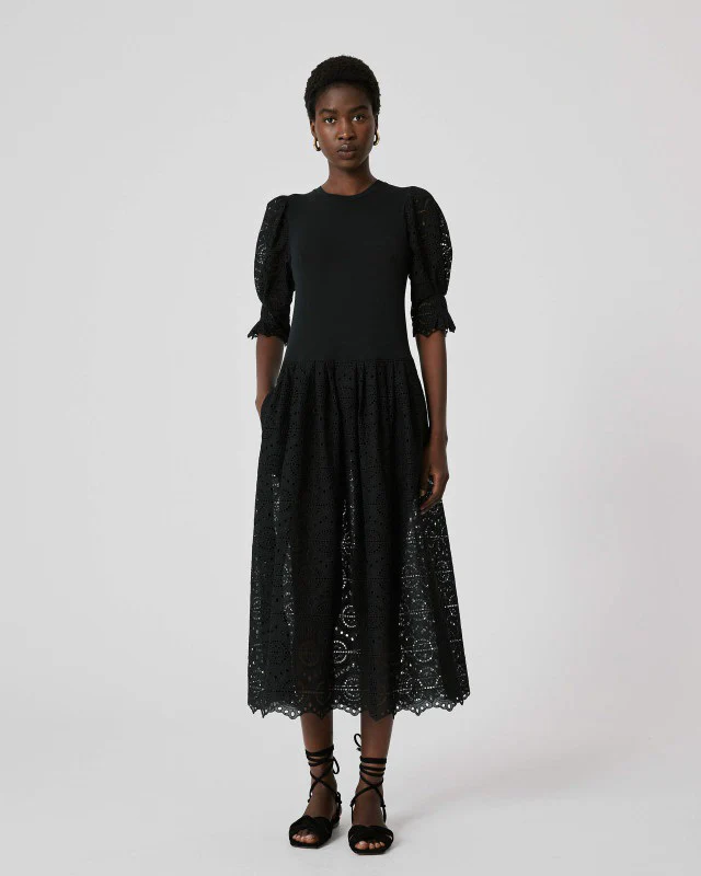 Model wearing a black midi dress with puff sleeves and eyelet skirt, standing against a light background.
