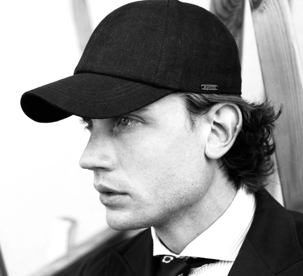 A black-and-white portrait of a man in profile wearing a dark cap, dressed in a suit and patterned tie.