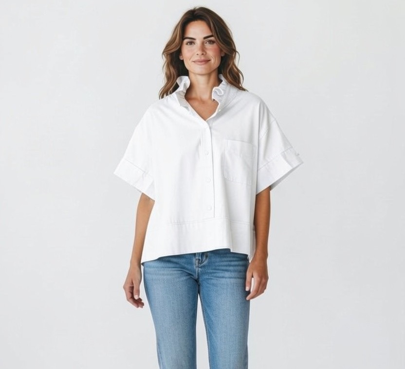 Woman wearing a loose white short-sleeve blouse and blue jeans, standing against a plain background with a relaxed, confident expression.