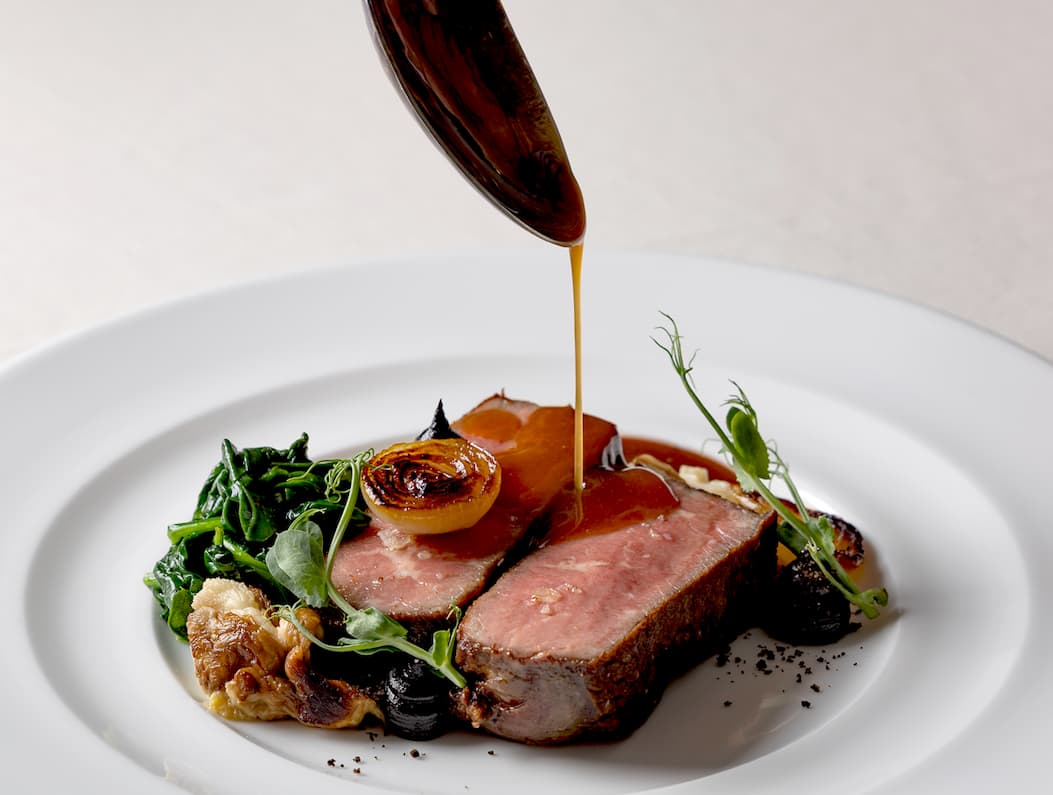 Elegant plated beef entrée with greens and roasted vegetables as a rich sauce is poured over the dish. Fearrington Village.