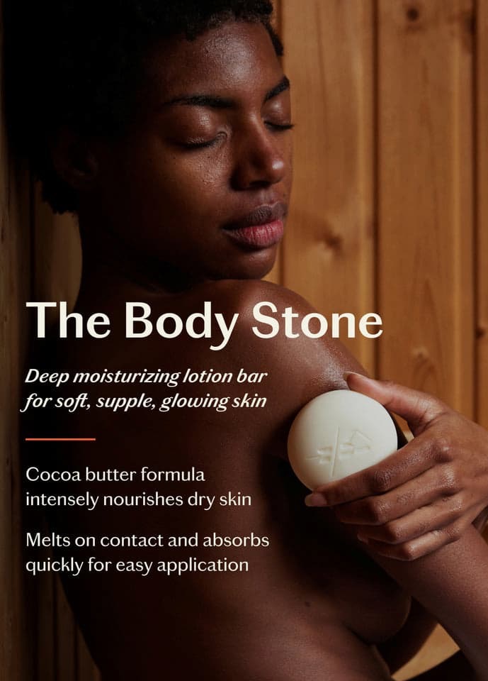 Person applying a round lotion bar to their shoulder with text describing “The Body Stone,” a deep moisturizing cocoa butter lotion bar for dry skin.