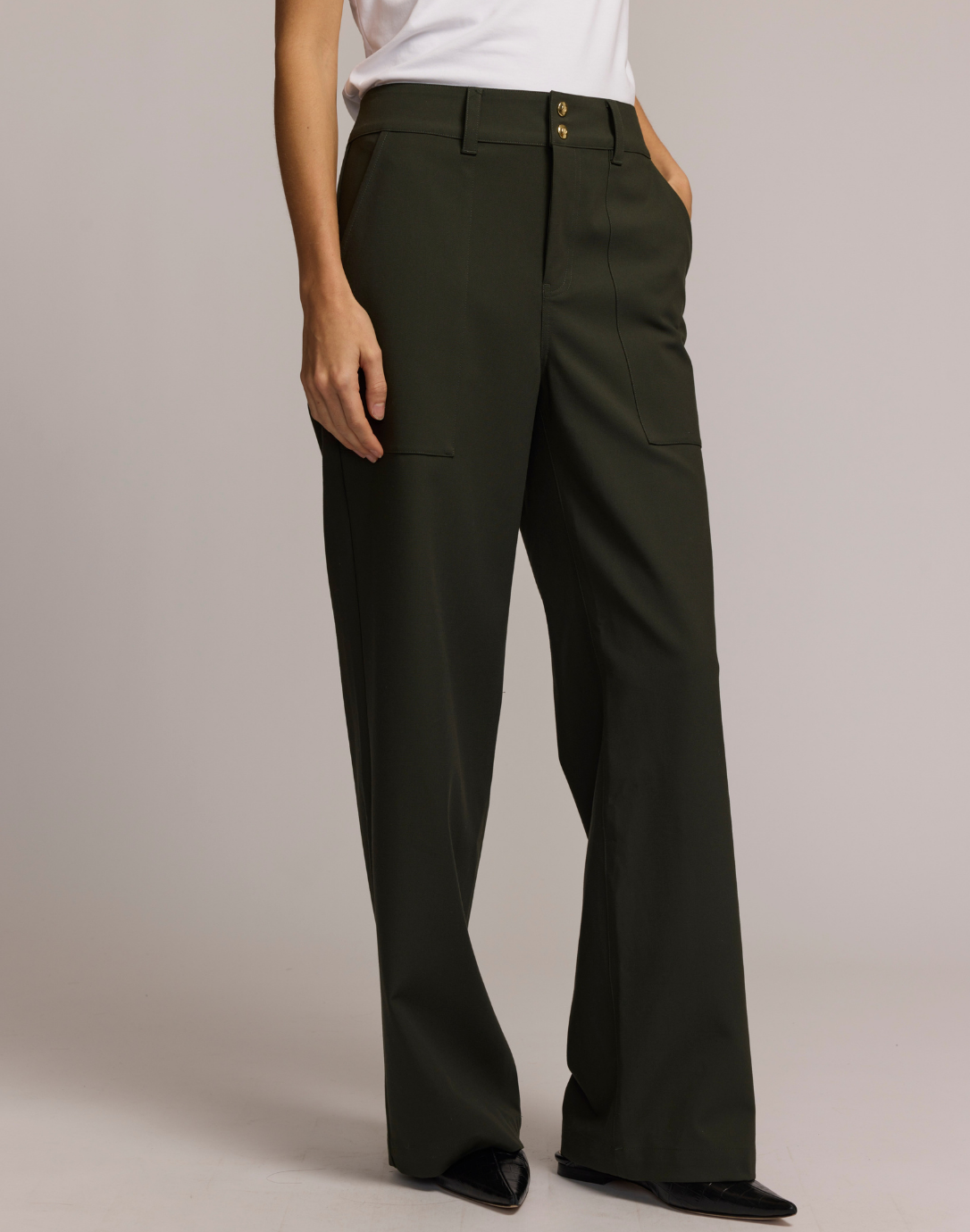 Model wearing high-waisted dark olive wide-leg trousers with front patch pockets and gold button details at the waist.