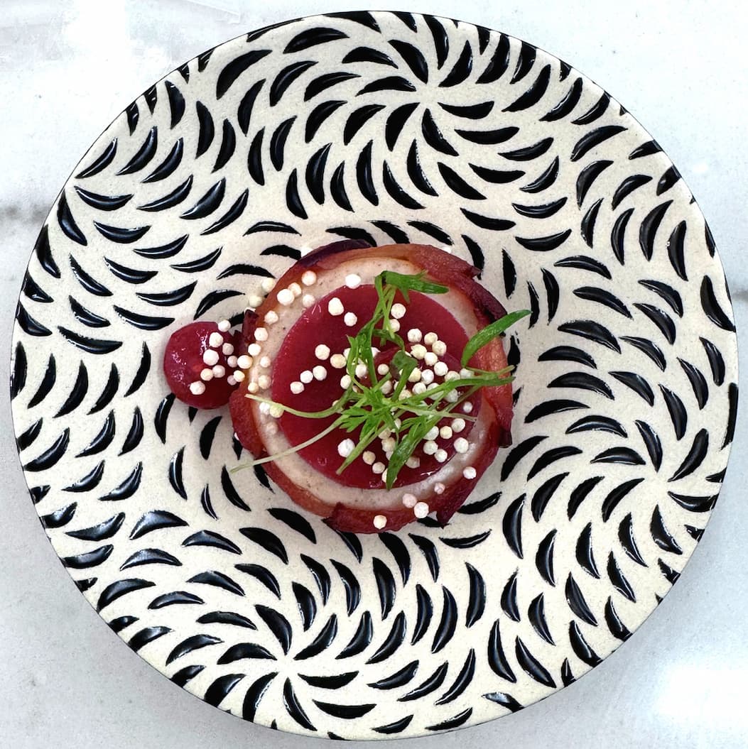 Elegant amuse-bouche with beet, mousse, crispy pearls, and microgreens on a patterned plate. Fearrington Village.