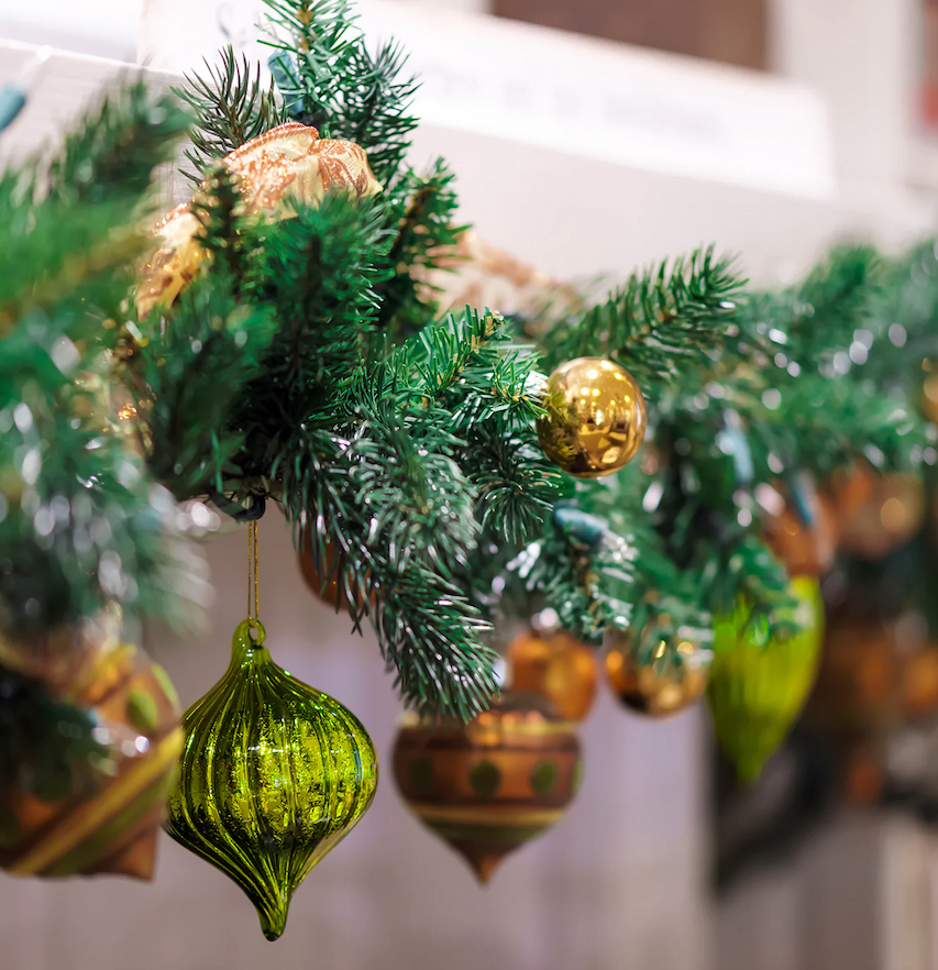 A festive garland of green pine branches decorated with gold and green ornaments hanging along a mantel.