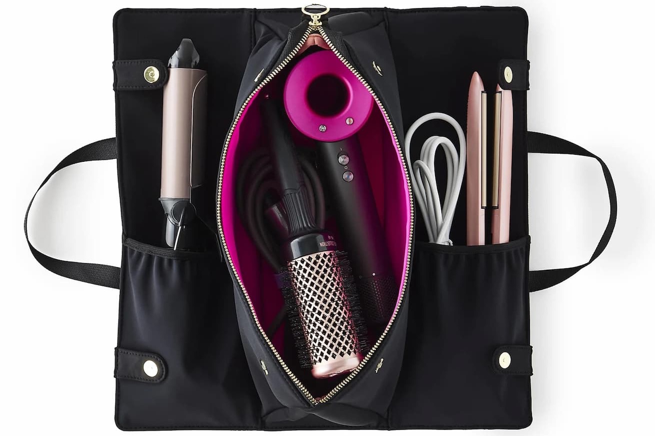 Black travel hair tool organizer with bright pink lining, holding a hair dryer, curling iron, flat iron, round brush, and cords in separate storage compartments.