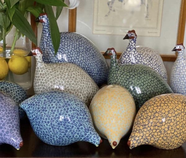 Colorful ceramic guinea fowl sculptures in assorted speckled patterns displayed with fresh lilies. Fearrington Village.