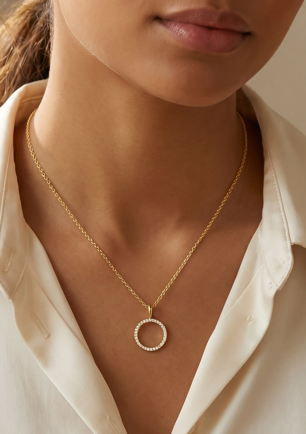 Close-up of a woman wearing a delicate gold necklace with a circular pavé diamond pendant, styled with a white collared blouse for an elegant, timeless look.