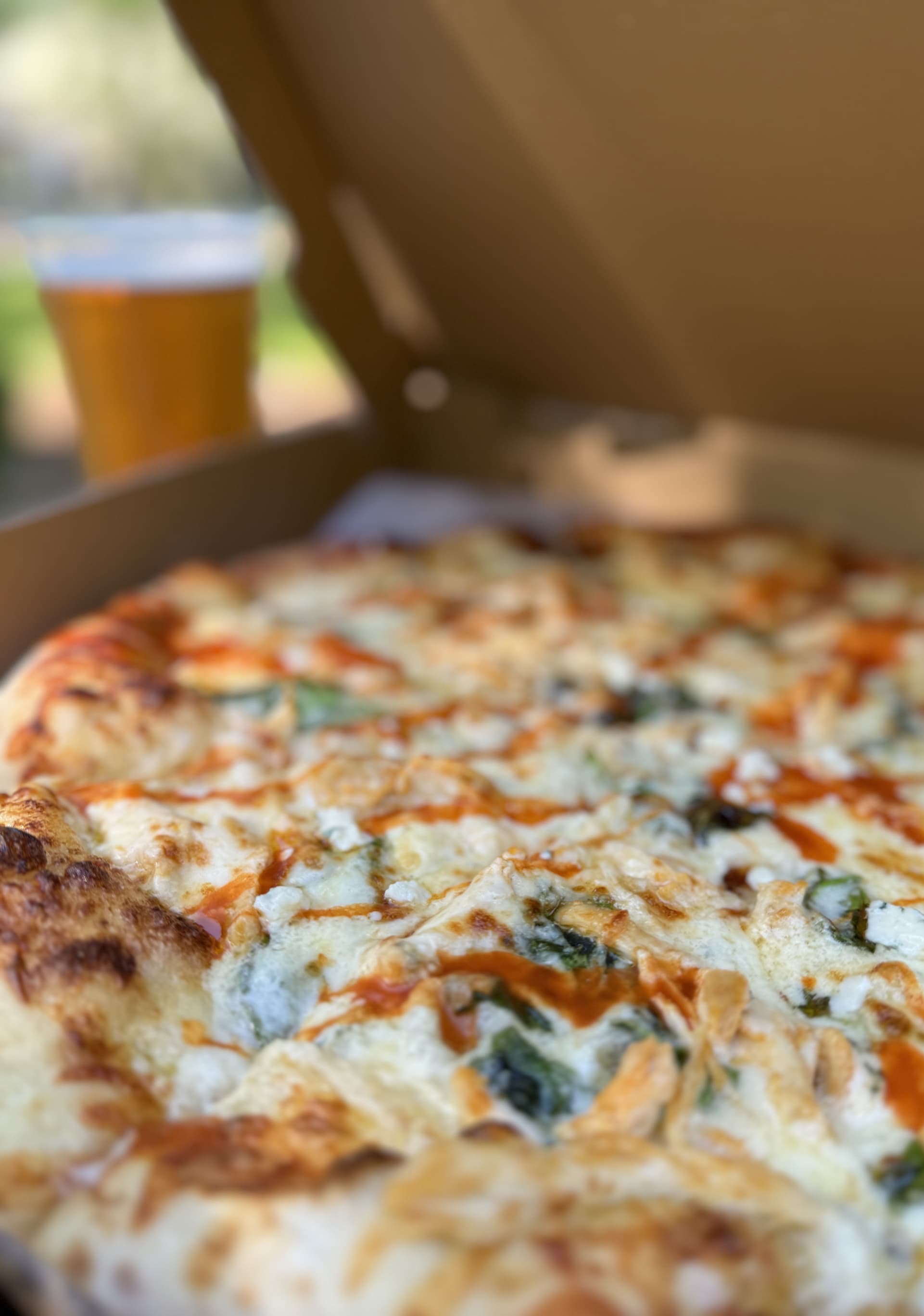 Wood-fired pizza topped with melted cheese, herbs, and hot honey, served with a cold beer. Fearrington Village.