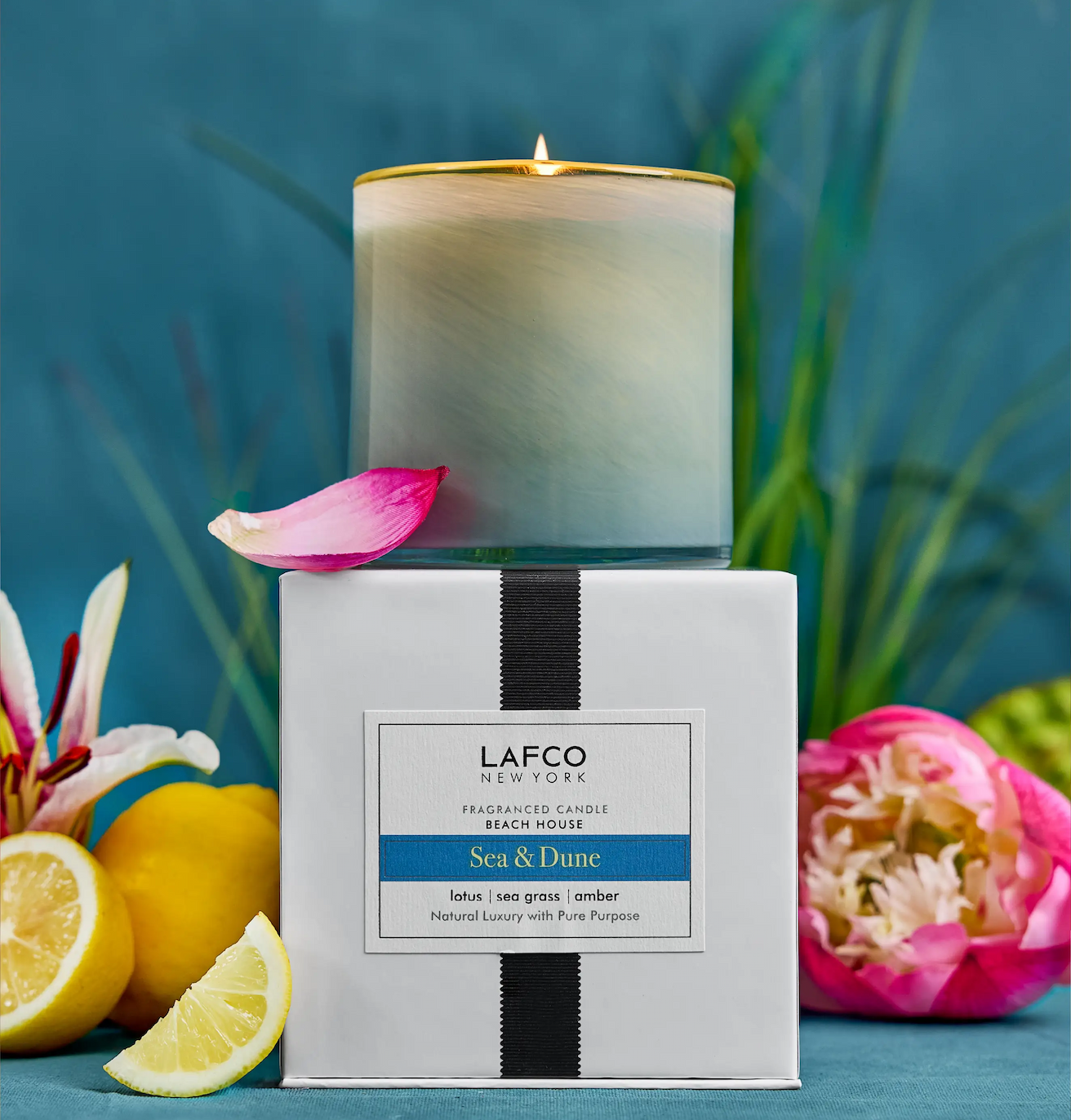 Frosted glass candle labeled “LAFCO New York Sea & Dune,” displayed on its box with lemon slices and flowers against a blue background.