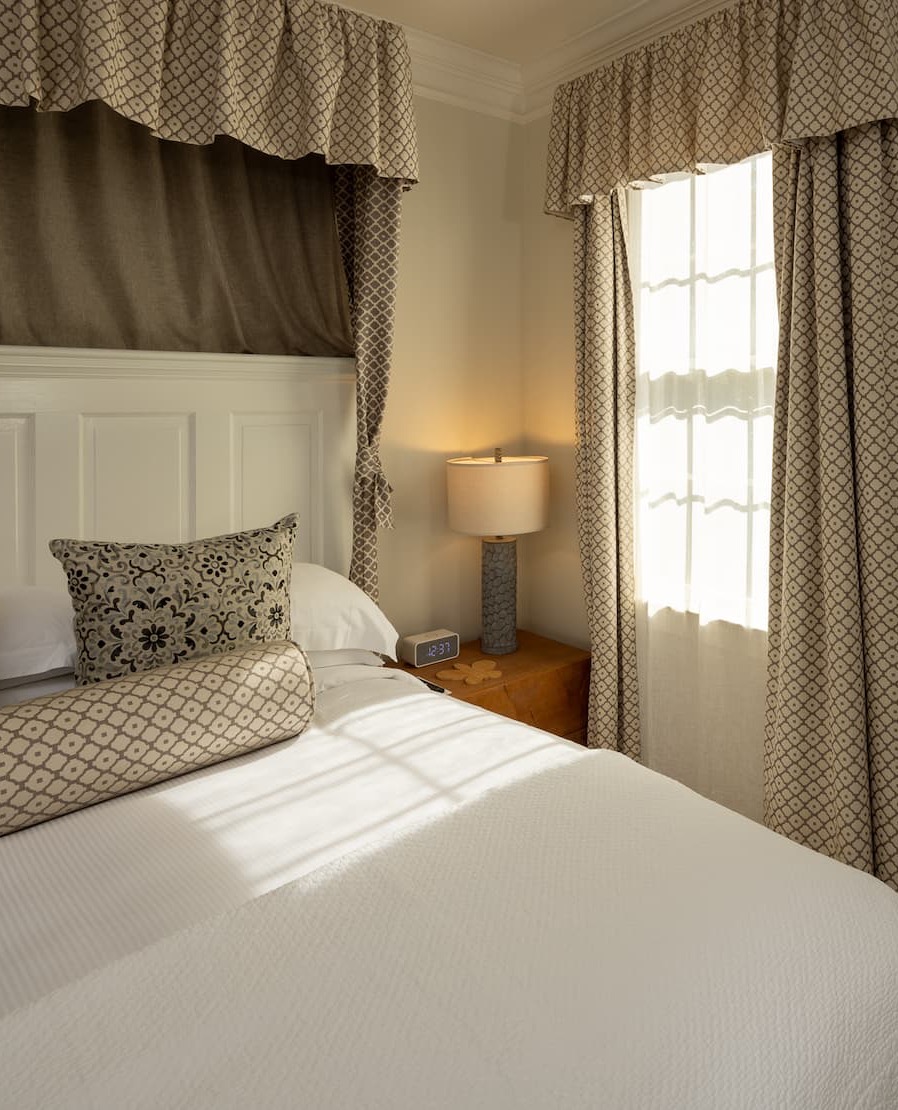 Cozy guest room with a canopy bed, patterned drapery, and warm natural light. Fearrington Village.