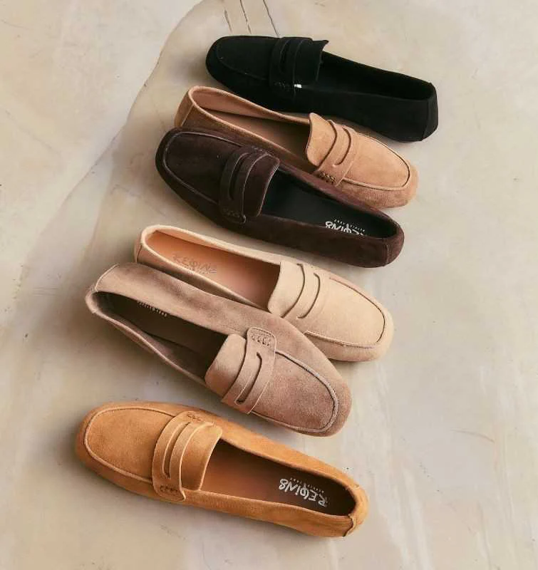 A diagonal arrangement of suede loafers in warm neutral tones including tan, blush, brown, and black on a light stone background.