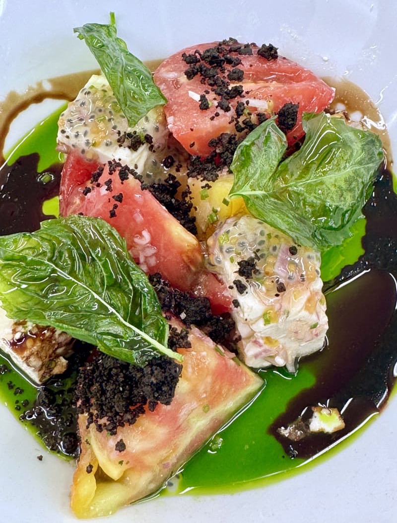 Heirloom tomato salad with basil leaves, creamy mozzarella, herb oil, balsamic reduction, and crisp savory crumbs. Fearrington Village.